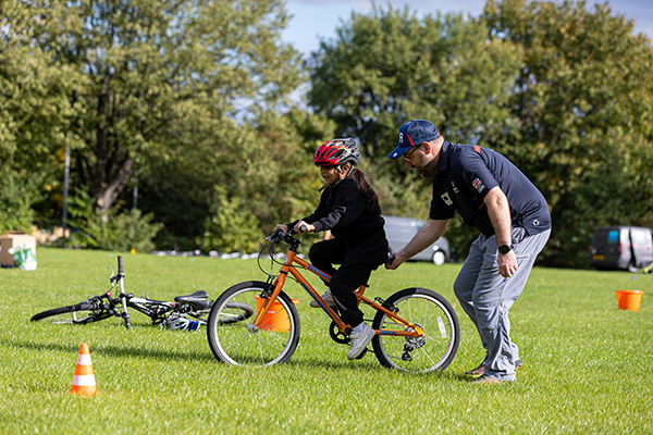 A volunteer giving a child a boost as she's riding her bike